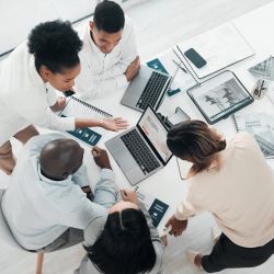 Business people, laptop and meeting in planning above for web design, strategy or brainstorming at the office. Top view of group designers working on computer for team project plan or idea on table